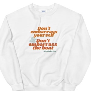 Op de afbeelding: Wit sweatshirt met een retro-stijl grafische afbeelding met de tekst "Don't embarrass yourself & Don't embarrass the boat - Captain Lee"