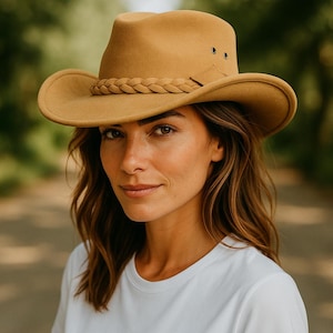 May include: A tan-coloured cowboy hat with a braided band and eyelets. The hat has a wide brim and a slightly curved crown. The hat is made of a felt-like material, suitable for outdoor wear.
