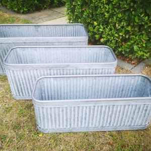 May include: Three galvanised metal planters in different sizes, stacked on top of each other. The planters are all rectangular and have a corrugated design.