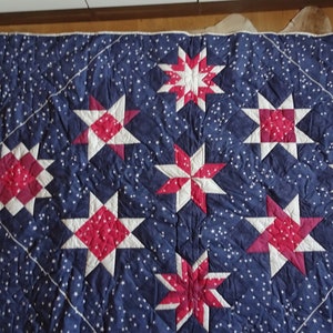 Könnte beinhalten: Eine blaue Steppdecke mit einem Muster aus weißen und roten Sternen. Die Steppdecke besteht aus Stoff mit einem weißen Sternenmuster auf blauem Hintergrund. Die Sterne sind in einem Gittermuster angeordnet.