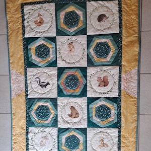 May include: A rectangular quilt featuring a yellow border with embroidered rose patterns. The center consists of alternating blocks: white squares with circular illustrations of woodland animals like a fox, hedgehog, skunk, and deer, and teal hexagons.