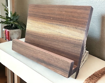 May include: A wooden book stand with a dark brown finish. The stand has a slanted surface for holding books or tablets and a lower shelf for additional support.