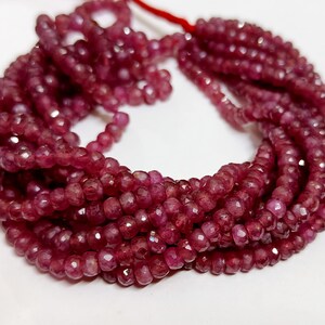 May include: A strand of ruby red faceted gemstone beads. The beads are small and round, and they are strung on a thin thread. The beads are a deep red color, and they have a shiny, polished finish.