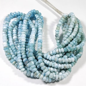 Puede incluir: Una colección de cuentas de piedras preciosas de color azul claro. Las cuentas facetadas están ensartadas, creando múltiples hebras. El color varía de azul pálido a medio, con una apariencia ligeramente translúcida. Las cuentas se utilizan probablemente para la fabricación de joyas.