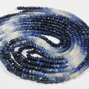 May include: A strand of blue sapphire beads in various shades of blue, from light to dark, with some white beads interspersed throughout.