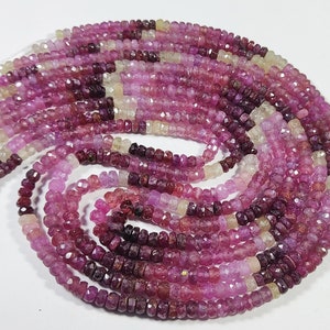 May include: A long strand of faceted rondelle beads in varying shades of pink, magenta, deep purple, and pale yellow. The small, circular gemstone beads are strung together on a thin, clear filament, arranged in a loose, swirling spiral pattern.