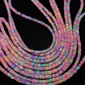 Puede incluir: Una hebra de cuentas de ópalo rosa con colores arcoíris iridiscentes. Las cuentas son pequeñas y redondas, y están enhebradas en un alambre fino. Hay varias hebras de cuentas en la imagen.