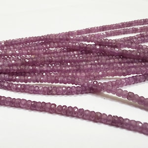 May include: A long strand of small, faceted, round, purple gemstone beads. The beads are uniform in size and shape, featuring a translucent quality with a reflective, multi-faceted surface that catches light across the entire length of the string.