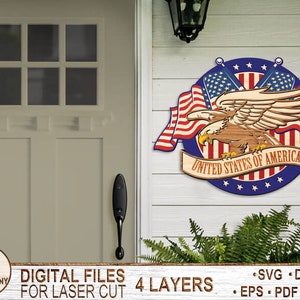 May include: A wooden cutout of an American bald eagle with wings spread, holding a banner that reads "United States of America". The eagle is surrounded by two crossed American flags and a blue circle with white stars. The cutout is designed for laser cutting and has four layers.