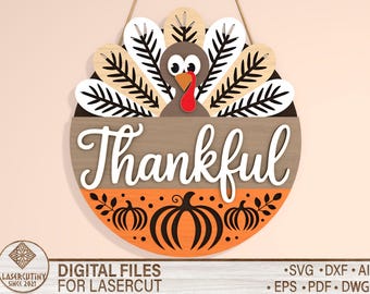May include: A round wooden Thanksgiving decoration featuring a turkey design and the word "Thankful" in white script. The turkey has a brown body, white and black feathers, and a red wattle. Orange pumpkins decorate the bottom.