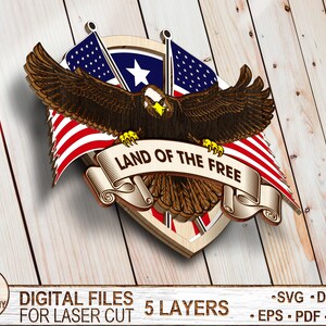 May include: A wooden cutout of an eagle with outstretched wings holding a scroll with the text "LAND OF THE FREE". The eagle is positioned in front of two American flags and a shield with a star.