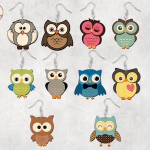 May include: Eight pairs of owl-shaped earrings with different colors and designs. The owls are made of wood and have painted details. The earrings are on a white background.