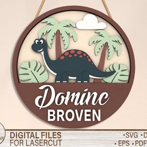 May include: A brown wooden circle with a dinosaur, palm trees, and leaves. The text "Dominc BROVEN" is written in white on the circle.
