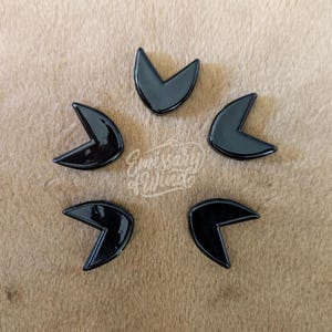 Op de afbeelding: Vijf zwarte pijlvormige keramische tegels gerangschikt in een cirkel op een bruin oppervlak.