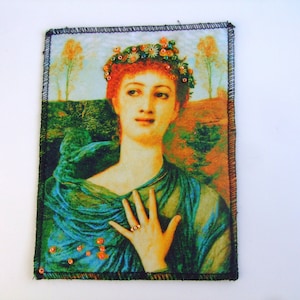 Peut inclure: Écusson rectangulaire en tissu représentant un portrait de style Renaissance d'une femme aux cheveux roux et à la couronne florale. Elle porte un vêtement drapé bleu-vert. L'écusson a une bordure cousue noire et des ornements orange.