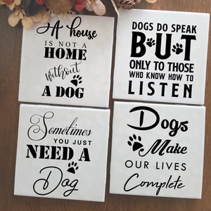 May include: Four white ceramic coasters with black text and paw prints. The coasters feature dog-themed quotes, such as "A house is not a home without a dog" and "Dogs make our lives complete."