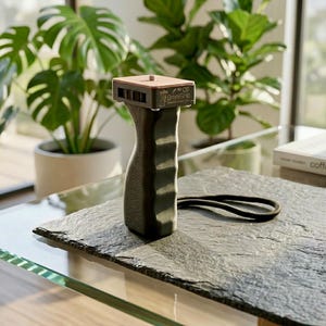 May include: A black Omnigrip camera handle with a brown top and a black wrist strap. The handle has a textured grip and a screw mount. The text "OmniGrip" is printed on the side.