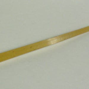 Puede incluir: Una cuchara de madera de color amarillo claro con un mango largo y rectangular y una cabeza triangular. La cuchara está hecha de una sola pieza de madera y tiene un acabado liso. La cuchara está diseñada para remover y servir alimentos.