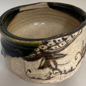 May include: A white ceramic mug with a black handle and the text "But First, Coffee" in a black, bold font. The mug is on a wooden surface.