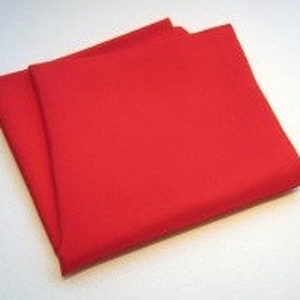 May include: Two folded, solid red pocket squares are stacked on a white surface. The fabric appears to be a smooth, woven material. The pocket squares are rectangular and have a clean, crisp appearance.