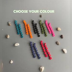 Könnte beinhalten: Ein Set langer Hängeohrringe mit einer Auswahl an Farben: Teal, Orange, Schwarz, Grün, Pink, Marineblau und Rot. Die Ohrringe bestehen aus mehreren runden Scheiben.