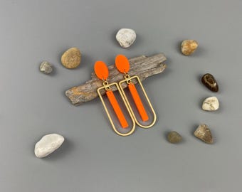 Peut inclure: Une paire de boucles d'oreilles géométriques orange et dorées. Les boucles d'oreilles présentent un long rectangle orange fin suspendu à un rectangle doré.