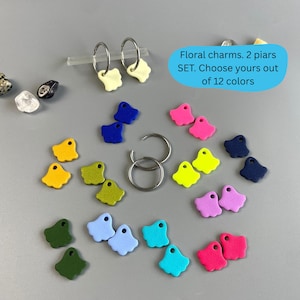 Könnte beinhalten: Eine Auswahl an bunten Blumenanhängern in Gelb-, Blau-, Rosa- und Grüntönen. Das Bild zeigt zwei Paar Creolen mit cremefarbenen Anhängern sowie lose Anhänger. Der Text auf dem Bild lautet: "Floral charms. 2 pairs SET. Choose yours out of 12 colors."