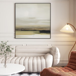 May include: A white sofa with a tufted design sits in a living room with a brown armchair, a floor lamp with a white shade, and a framed abstract painting on the wall.