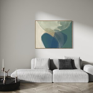 May include: Abstract art print with a blue, green, and white color scheme. The print is framed in a light wood frame and is hanging on a white wall above a white sofa.