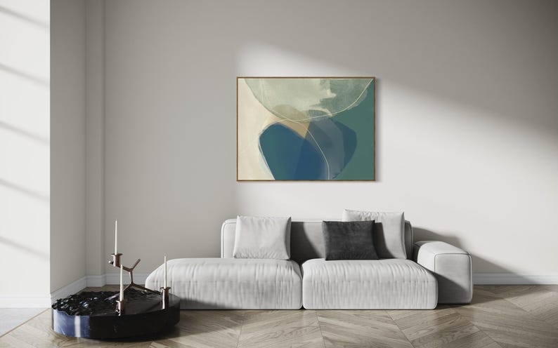May include: Abstract art print with a blue, green, and white color scheme. The print is framed in a light wood frame and is hanging on a white wall above a white sofa.