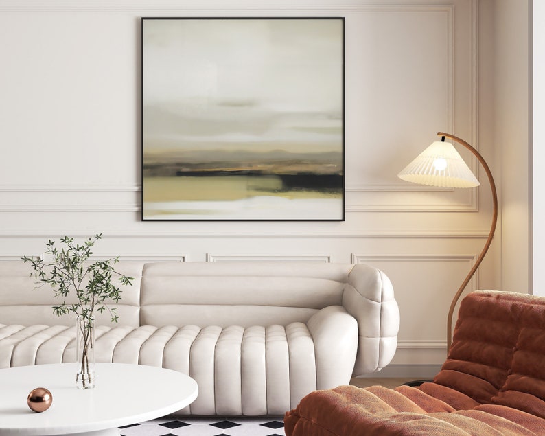 May include: A white sofa with a tufted design sits in a living room with a brown armchair, a floor lamp with a white shade, and a framed abstract painting on the wall.