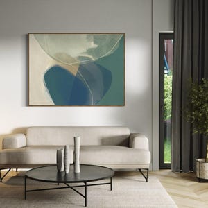 May include: A living room interior with a light gray sofa, a black coffee table, and a framed abstract painting on the wall. The painting features a blue and green abstract design. There are two potted plants in the room, one with green leaves and the other with a white pot.