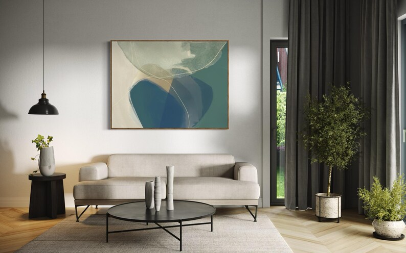 May include: A living room interior with a light gray sofa, a black coffee table, and a framed abstract painting on the wall. The painting features a blue and green abstract design. There are two potted plants in the room, one with green leaves and the other with a white pot.