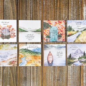 May include: Eight square watercolour art prints featuring inspirational quotes and landscape scenes. The prints depict a window, mountains, a lake, and a canoe. The colour palette includes blues, greens, and browns.