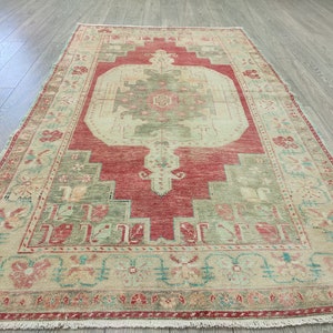 May include: A vintage rug with a central medallion in shades of beige, red, and green. The rug has a geometric pattern with floral motifs and a fringed border.