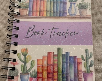 Puede incluir: Un cuaderno de seguimiento de lectura con encuadernación en espiral que presenta una ilustración en acuarela de dos estantes llenos de libros coloridos, cactus en macetas y un jarrón con lavanda. La banda central morada muestra el texto Book Tracker.