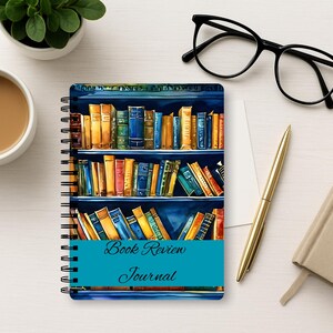Puede incluir: Un cuaderno de espiral con una colorida ilustraci&oacute;n de estanter&iacute;as llenas de varios libros en su portada. Una banda horizontal de color verde azulado en el centro muestra el texto Book Review Journal en una fuente cursiva oscura.