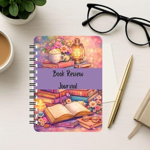 Puede incluir: Un diario de rese&ntilde;as de libros con encuadernaci&oacute;n en espiral que presenta una colorida ilustraci&oacute;n de libros apilados, una linterna, una taza y flores. Una banda horizontal morada en el centro muestra el texto Book Review Journal en letra simple.