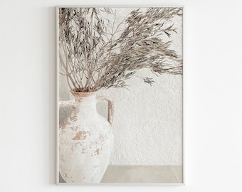 May include: A white ceramic vase with a rustic, weathered finish holds a bouquet of dried, light brown branches. The vase is set against a white textured wall.