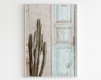 May include: A framed print of a cactus plant growing next to a weathered, light blue wooden door.