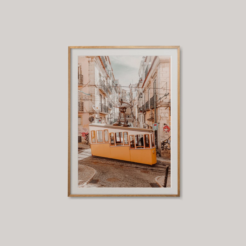 May include: A yellow and white vintage tram car traveling up a steep, narrow street in a city. The street is lined with buildings on both sides, and the tram car is in the center of the image.