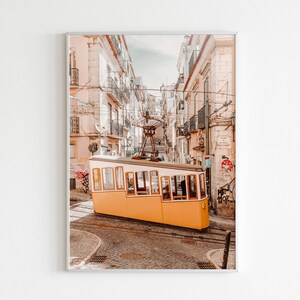 May include: A yellow vintage tram travels up a steep, narrow street in Lisbon, Portugal. The street is lined with buildings in shades of beige and white.