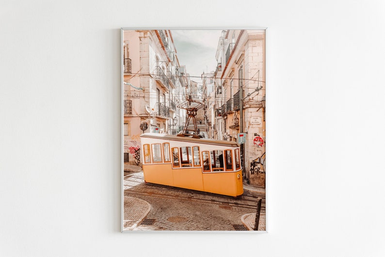 May include: A yellow vintage tram travels up a narrow street in Lisbon, Portugal. The tram is surrounded by tall, colorful buildings with balconies.