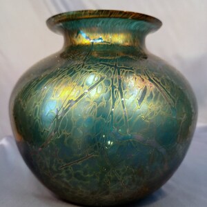Könnte beinhalten: Eine tealfarbene, irisierende Glasvase mit rundem Korpus und einer weiten Öffnung. Die Vase hat ein goldenes und braunes Muster.