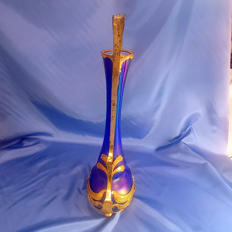 May include: A tall, iridescent blue glass vase with gold accents and a decorative handle. The vase has a bulbous base and a slender neck.