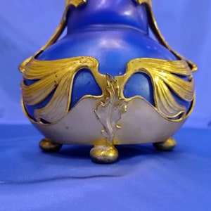 May include: A blue and gold ceramic vase with an ornate design. The vase has a round body and a wide mouth. It is decorated with gold leaf and has three feet.