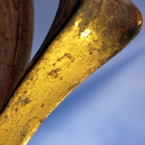 May include: Close-up of a gold-colored metal object with a textured surface. The object has a curved shape and appears to be part of a larger piece.
