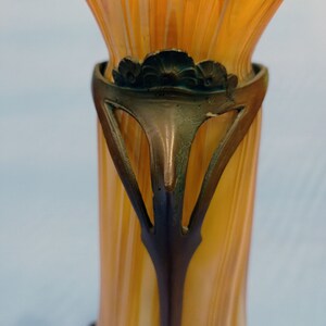Puede incluir: Un jarr&oacute;n de vidrio alto de color &aacute;mbar con una base de metal bronce decorativa. La base presenta un dise&ntilde;o floral y recortes intrincados.