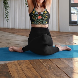 May include: A woman wearing a black sports bra with a floral print and black leggings sits on a blue yoga mat.