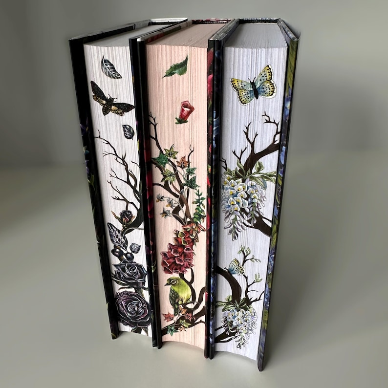 May include: Three hardcover books with floral and insect designs on the spines. The spines are white, pink, and blue with black trim. The designs include butterflies, birds, and flowers.